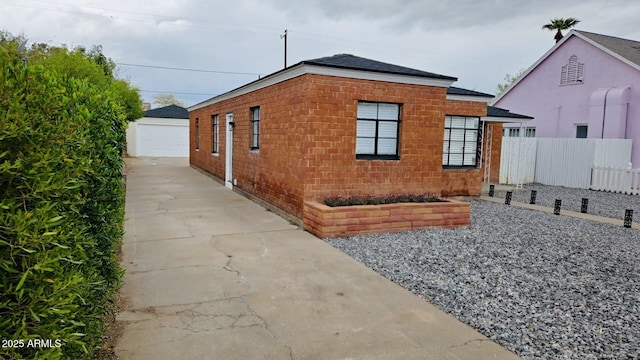 view of side of property featuring an outbuilding, fence, concrete driveway, a garage, and brick siding