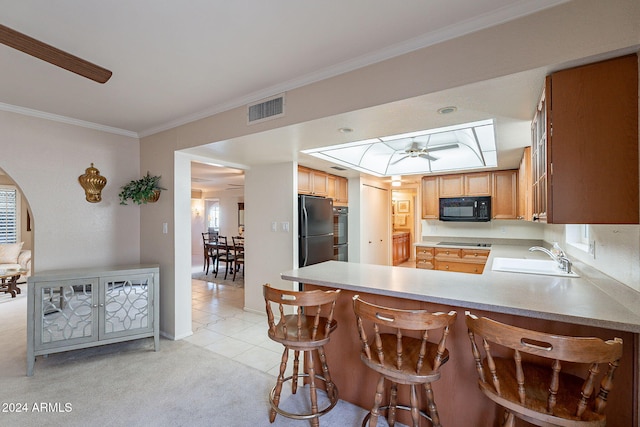 kitchen with kitchen peninsula, ornamental molding, sink, black appliances, and light tile patterned floors