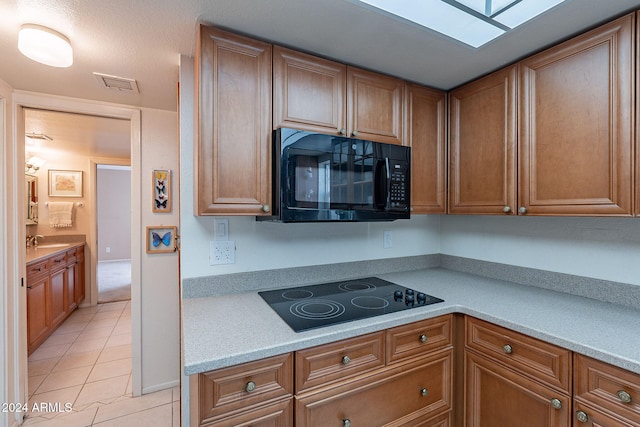 kitchen with light tile patterned floors, sink, a skylight, and black appliances