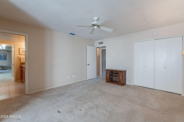 unfurnished bedroom featuring ceiling fan, light colored carpet, ensuite bathroom, and a closet