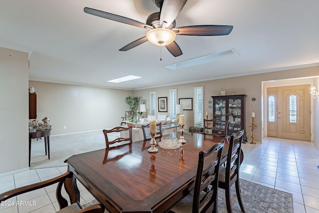 tiled dining space with ceiling fan, crown molding, and a skylight