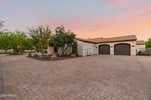 mediterranean / spanish house featuring decorative driveway, a tiled roof, an attached garage, and stucco siding