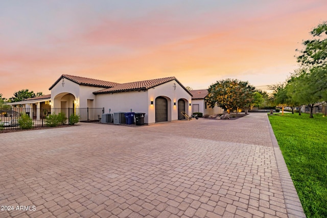 mediterranean / spanish house featuring a tile roof, fence, decorative driveway, central air condition unit, and stucco siding