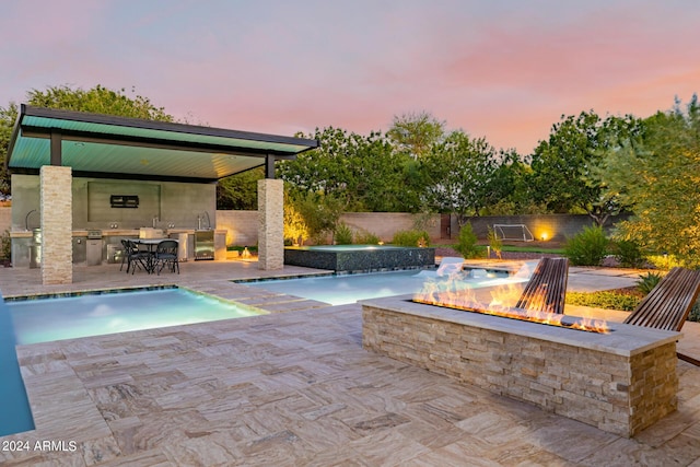 pool at dusk featuring a fenced in pool, an outdoor kitchen, an outdoor fire pit, a patio area, and fence private yard