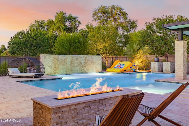 pool at dusk with a fire pit, a patio area, a fenced backyard, and a fenced in pool