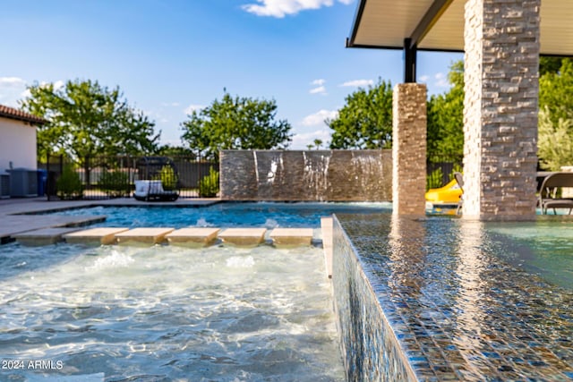 view of swimming pool featuring a pool with connected hot tub and fence