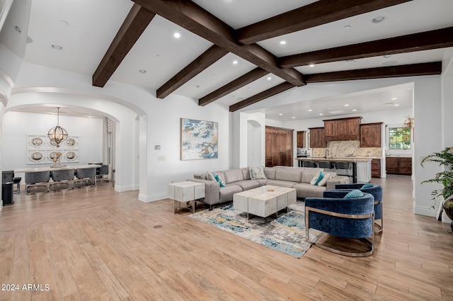 living area featuring arched walkways, vaulted ceiling with beams, a chandelier, and light wood-style floors