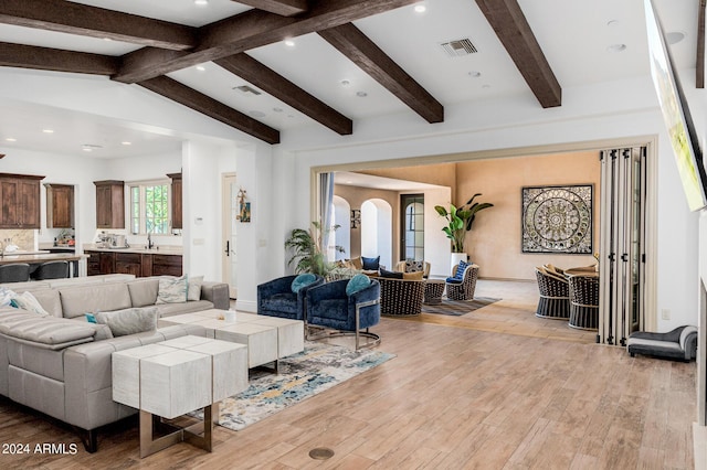 living room with vaulted ceiling with beams, light wood-style floors, visible vents, and arched walkways