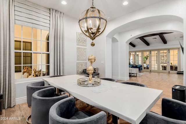 dining area with light wood-type flooring, an inviting chandelier, arched walkways, and beamed ceiling