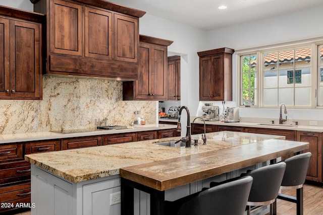 kitchen featuring stovetop, an island with sink, a sink, and tasteful backsplash