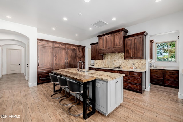 kitchen featuring arched walkways, a sink, visible vents, light wood-style floors, and tasteful backsplash