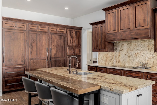 kitchen featuring light stone counters, a kitchen breakfast bar, dark wood-type flooring, a sink, and backsplash