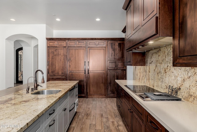 kitchen with paneled built in fridge, decorative backsplash, a sink, light wood-type flooring, and under cabinet range hood