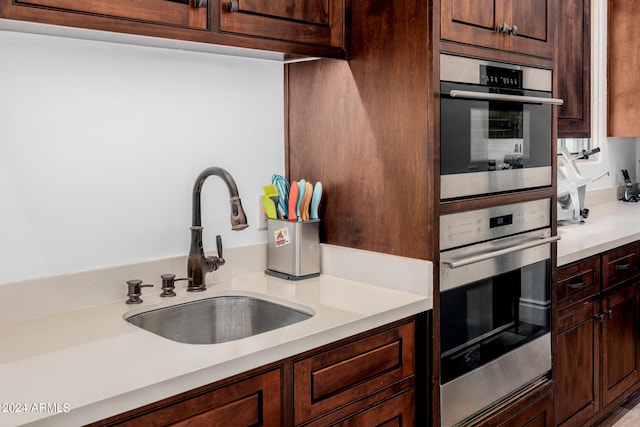 kitchen featuring light countertops, dark brown cabinets, double oven, and a sink