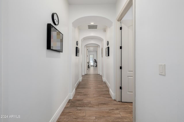 hallway with arched walkways, light wood finished floors, visible vents, and baseboards