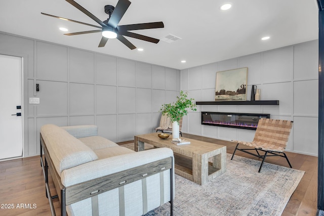 4910 E Shaw Butte Dr, Scottsdale, AZ 85254 - living room with a decorative wall, a ceiling fan, wood finished floors, a glass covered fireplace, and recessed lighting