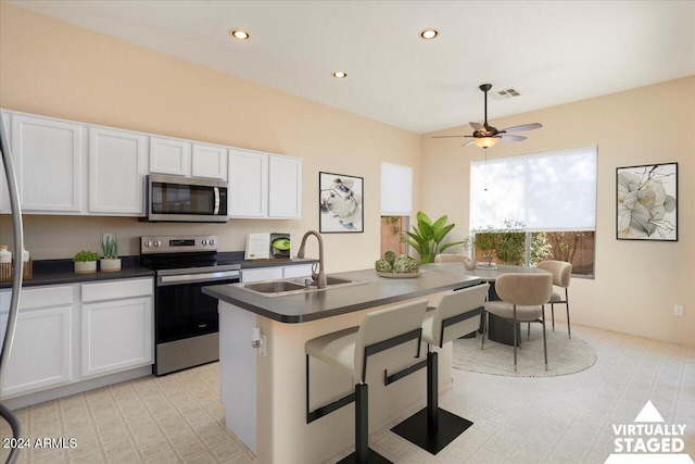 kitchen with appliances with stainless steel finishes, ceiling fan, sink, a center island with sink, and white cabinets