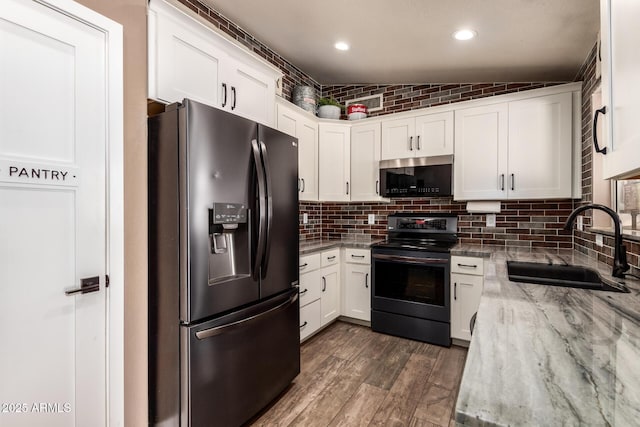 kitchen featuring refrigerator with ice dispenser, a sink, black electric range oven, and white cabinets