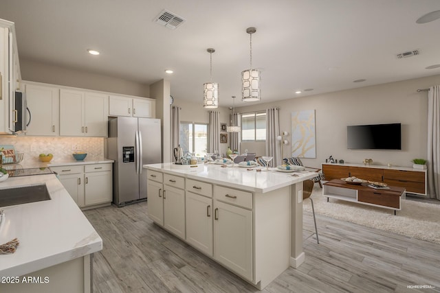 kitchen with light hardwood / wood-style flooring, a center island, decorative light fixtures, stainless steel appliances, and white cabinetry