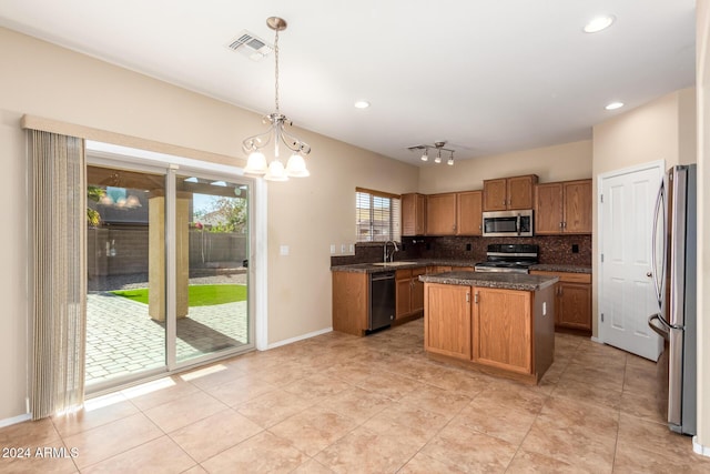 kitchen featuring appliances with stainless steel finishes, dark stone counters, pendant lighting, an inviting chandelier, and a kitchen island