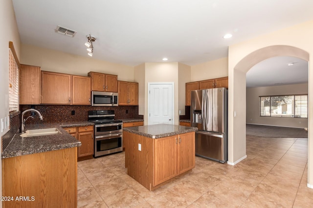 kitchen with sink, stainless steel appliances, backsplash, dark stone countertops, and a kitchen island