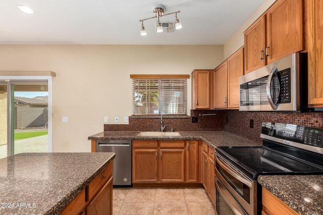 kitchen featuring backsplash, sink, dark stone countertops, light tile patterned floors, and appliances with stainless steel finishes