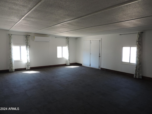 unfurnished room with a wall mounted air conditioner, a textured ceiling, and a wealth of natural light