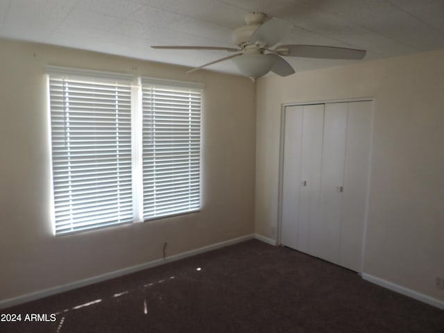 unfurnished bedroom featuring a closet, multiple windows, dark carpet, and ceiling fan