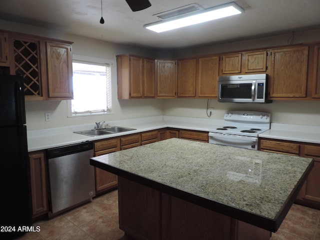 kitchen featuring sink, light stone countertops, a center island, light tile patterned flooring, and appliances with stainless steel finishes