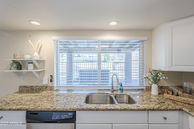 kitchen featuring light stone counters, dishwashing machine, sink, and white cabinets