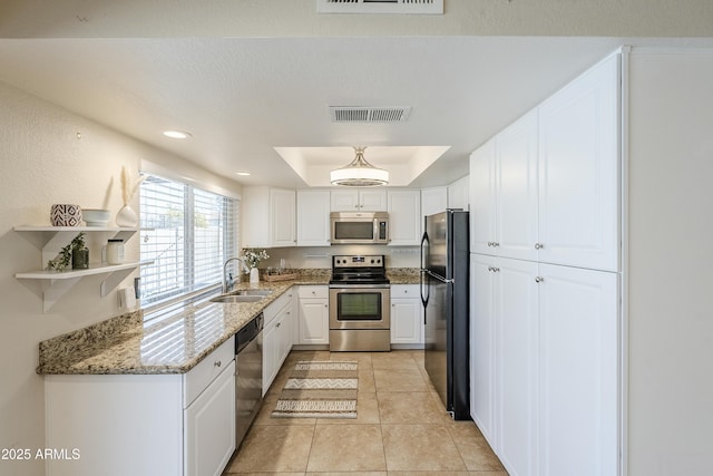 kitchen with appliances with stainless steel finishes, stone countertops, sink, white cabinets, and a raised ceiling