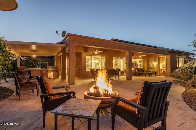 patio terrace at dusk with an outdoor kitchen, ceiling fan, a grill, and an outdoor living space with a fire pit