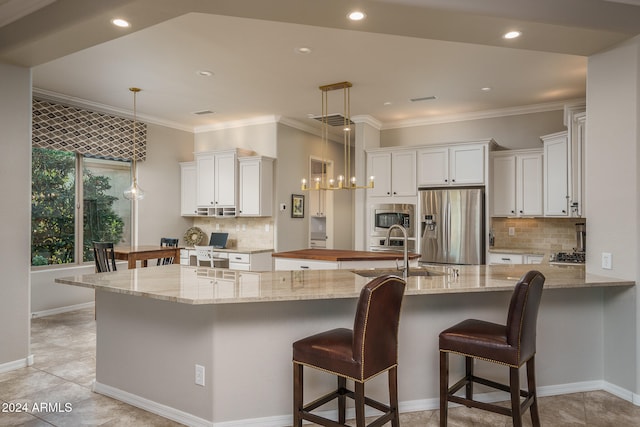 kitchen with white cabinets, stainless steel appliances, hanging light fixtures, and an island with sink