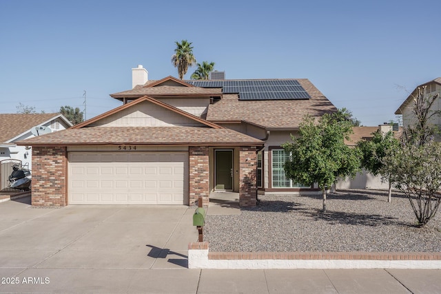 traditional-style house featuring a garage, brick siding, concrete driveway, roof with shingles, and roof mounted solar panels