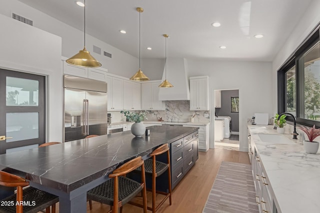 kitchen featuring stainless steel built in refrigerator, sink, custom exhaust hood, white cabinetry, and pendant lighting