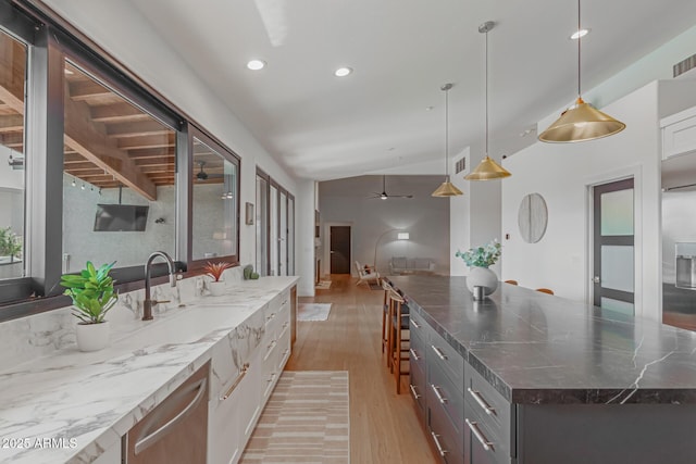 kitchen with a kitchen island, pendant lighting, dark stone countertops, stainless steel dishwasher, and light hardwood / wood-style floors