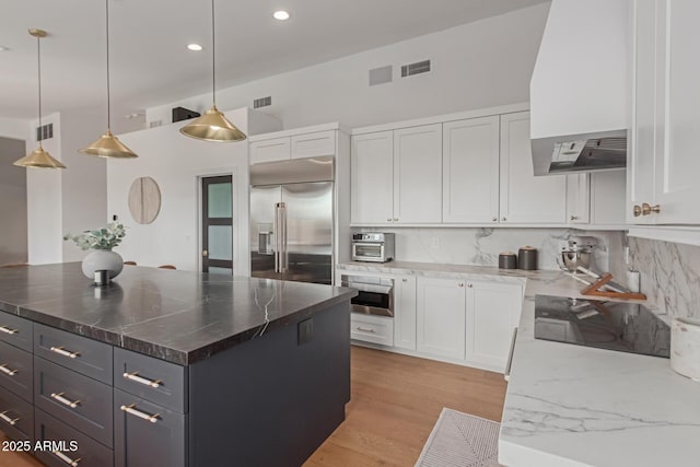 kitchen with pendant lighting, built in refrigerator, a center island, white cabinets, and dark stone counters