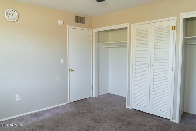 unfurnished bedroom with two closets and dark colored carpet