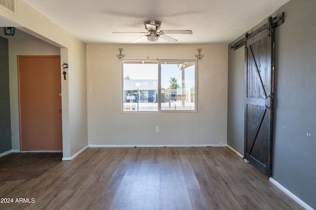 unfurnished room featuring a barn door, dark wood-type flooring, and ceiling fan