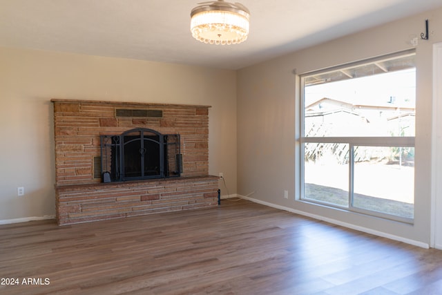 unfurnished living room featuring a stone fireplace, plenty of natural light, and hardwood / wood-style floors