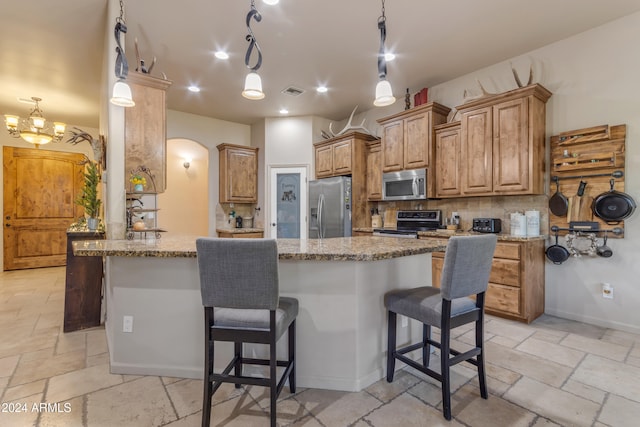 kitchen with light stone countertops, appliances with stainless steel finishes, a kitchen bar, an inviting chandelier, and kitchen peninsula