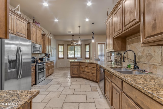 kitchen with light stone countertops, appliances with stainless steel finishes, sink, pendant lighting, and backsplash