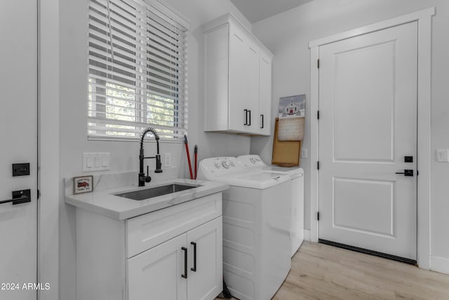 laundry area with cabinets, sink, separate washer and dryer, and light hardwood / wood-style floors