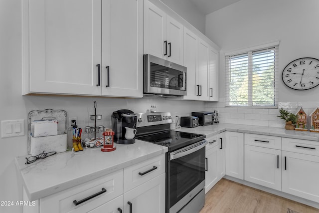 kitchen with light stone counters, white cabinets, appliances with stainless steel finishes, and light wood-type flooring