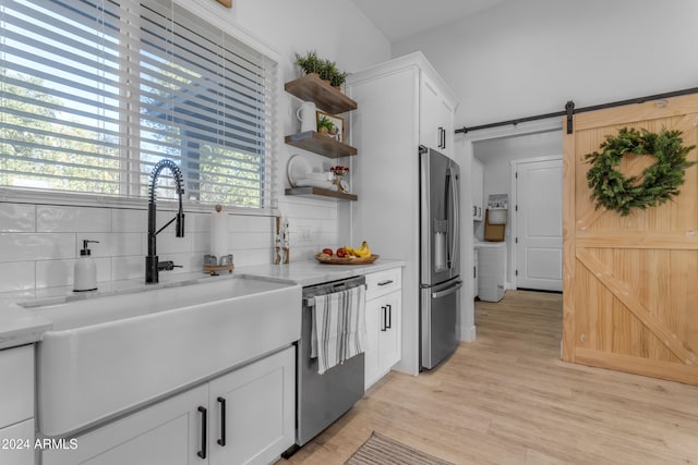 kitchen with appliances with stainless steel finishes, sink, white cabinets, tasteful backsplash, and a barn door