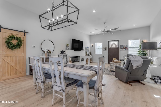 dining area with light hardwood / wood-style floors, ceiling fan with notable chandelier, and a barn door