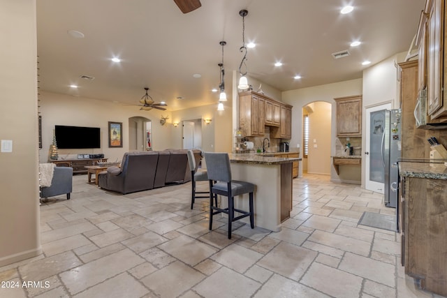 kitchen with ceiling fan, sink, light stone counters, and a kitchen bar