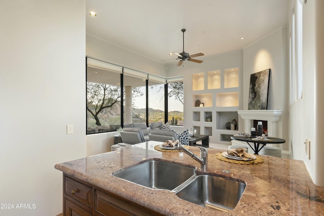 kitchen with built in shelves, light stone counters, sink, and ceiling fan