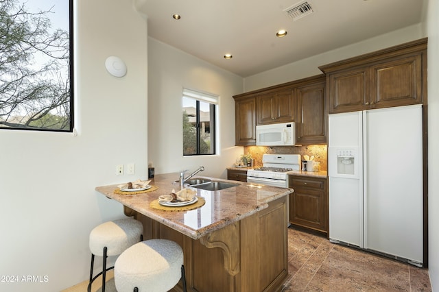 kitchen featuring white appliances, a kitchen breakfast bar, sink, light stone countertops, and tasteful backsplash