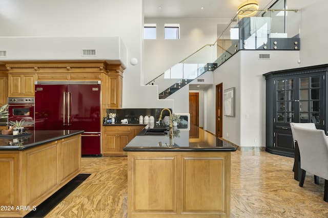 kitchen featuring a center island with sink, oven, sink, a towering ceiling, and stainless steel built in refrigerator